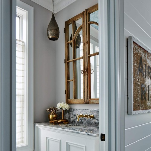 Entrance to powder room, white walls with striking marble countertop and brass accents